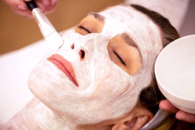 Kozmetik güzellik maskesini kapatın. Kadınların yüzüne bir fırçayla sürülüyor.