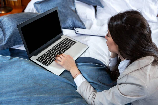 Бізнес-леді перевіряє свій ноутбук, сидячи в ліжку — стокове фото