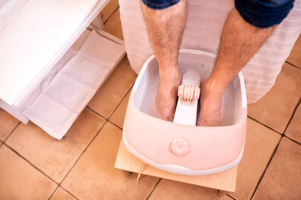 Feet of a young man sunk in a foot bath tub, pedicure concept