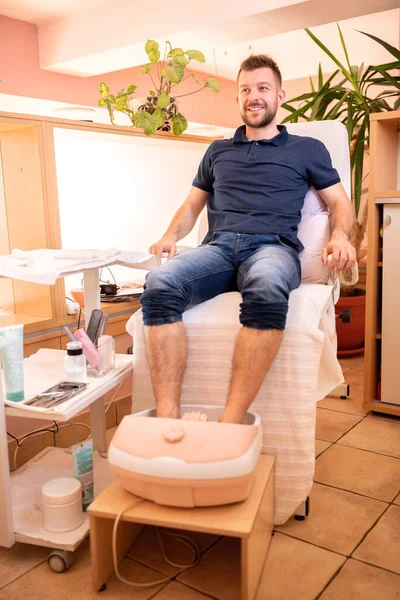 Young man in a pedicure salon sitting with his feet sunk in a spa bath