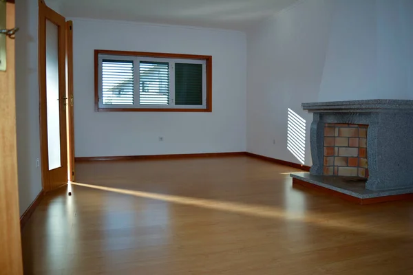 Boş bir oturma odası, bir şömine, bir pencere ve yerde ve duvarda güneş yansımalarını gösteren bir kapı.