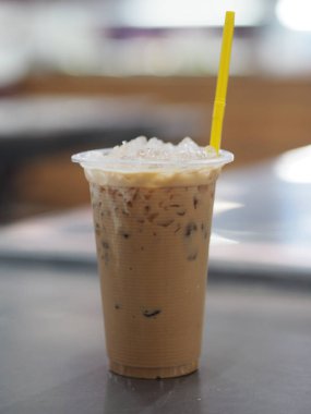 Açık plastik bardakta buzlu kahve. Masanın üzerinde sarı renkli plastik tüpler var.