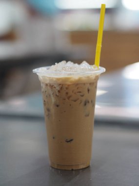 Açık plastik bardakta buzlu kahve. Masanın üzerinde sarı renkli plastik tüpler var.