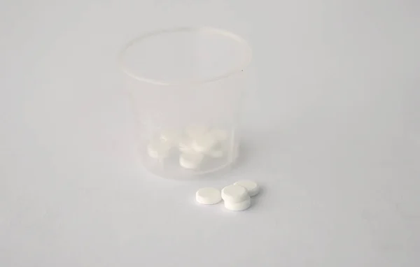 white color tablets pills capsule heap mix therapy drugs with clear plastic glass on white paper