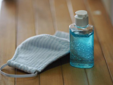 Plastik şişede el yıkama jeli, masa başı ahşap arka plan tozu üzerinde Mavi Maske kumaşı ve sonra mikroplar 2.5, virüs covid 19, Uv