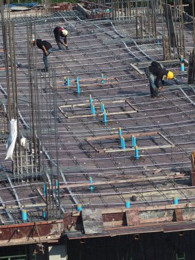 Erkek işçiler beton döşemeye hazırlanmak için demir bağlıyor.