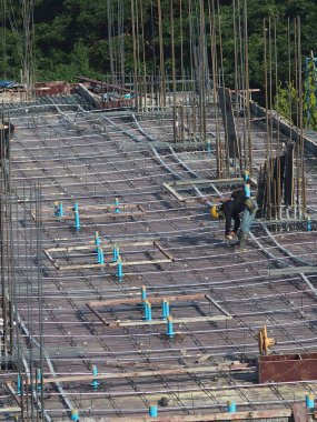Erkek işçiler beton döşemeye hazırlanmak için demir bağlıyor.