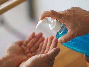 Kadının eli alkol jeli pompasının şişesine basıyor. Kolona virüsünü korumak için kiri temizlemek için başka bir ele verin.