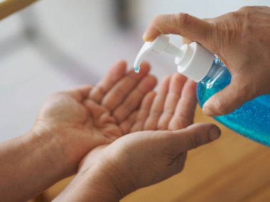 Kadının eli alkol jeli pompasının şişesine basıyor. Kolona virüsünü korumak için kiri temizlemek için başka bir ele verin.
