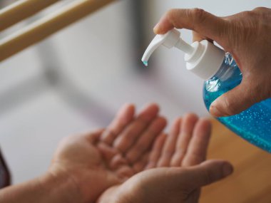Kadının eli alkol jeli pompasının şişesine basıyor. Kolona virüsünü korumak için kiri temizlemek için başka bir ele verin.