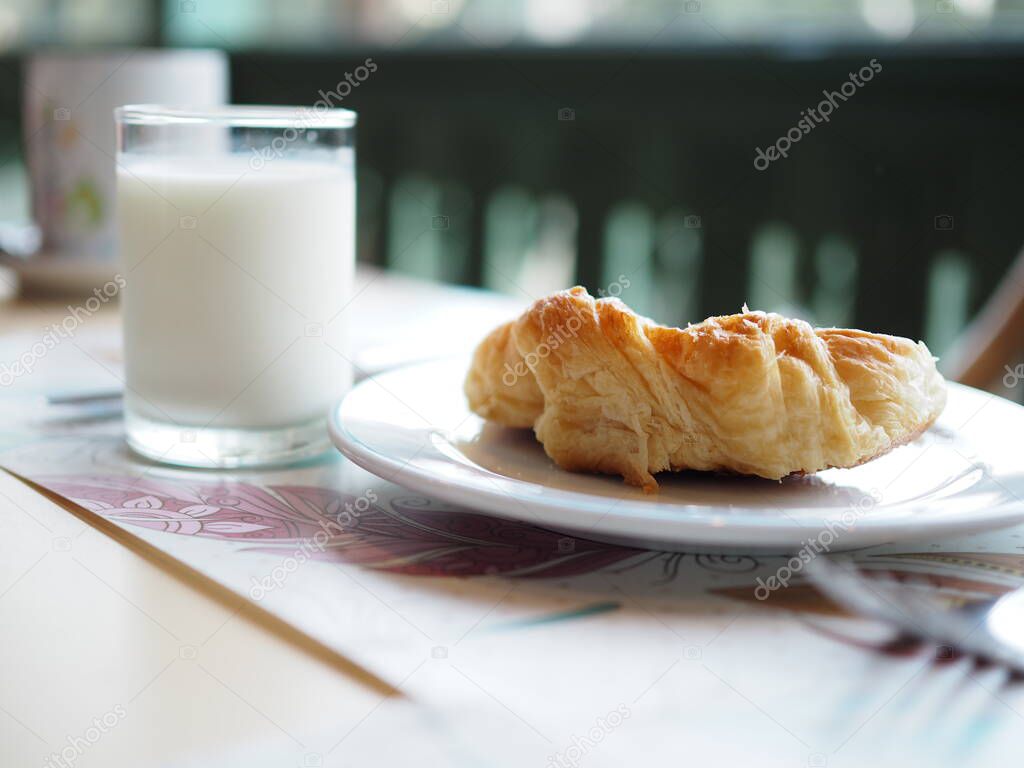 Croissant on white dish and fresh milk in clear glass on the table