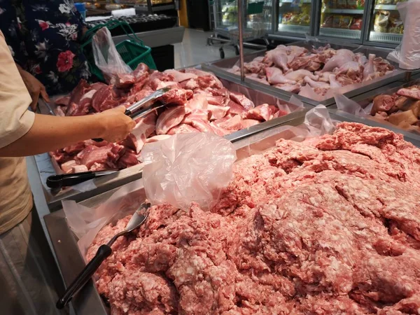 Woman catching ground pork on a stainless steel tray in supermarket