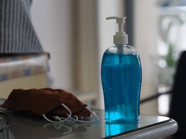 El dezenfektanı ve kumaş maskesi masada, jelatin ile saf plastik şişedeki jelatin karışımı temiz plastik şişeyle birlikte temiz çamaşır yıkama, mikropların bulaşıcı corona virüsünü koruması için kirli çamaşır yıkama, covid-19