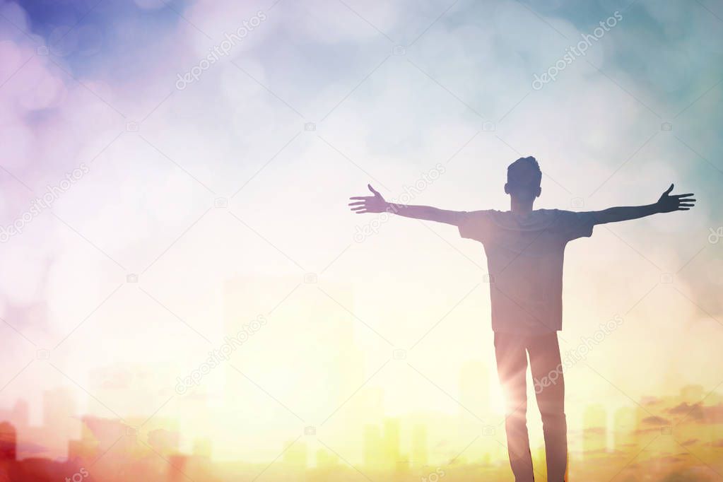 Silhouette of man with raised hands over blur city concept for religion, worship, prayer and praise.