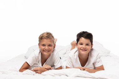 two happy brothers lying on bed and smiling at camera isolated on white clipart