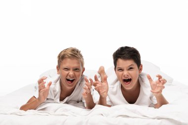 two brothers grimacing and showing frightening gestures while lying on bed isolated on white clipart