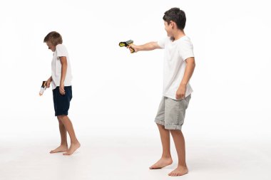  boy aiming with toy gun at scared brother on white background clipart