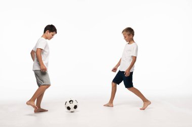 Beyaz arka planda futbol oynayan pijamalı iki kardeş.