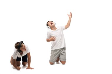 Heyecanlı çocuk kulaklıkla müzik dinliyor ve beyaz arka planda gülen kardeşin yanında şarkı söylüyor.