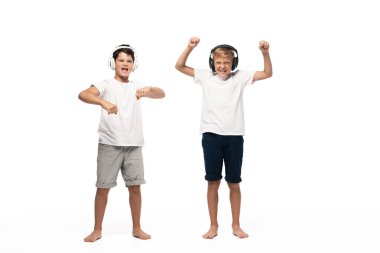 two cheerful brothers listening music in headphones and dancing on white background clipart