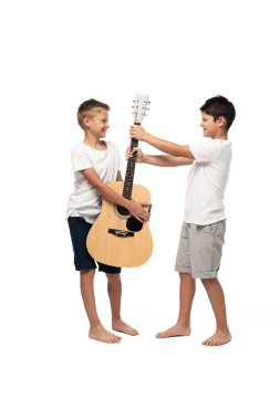 Yaramaz çocuk beyaz arka planda kardeşinin gitarını çalıyor.