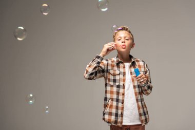 boy in checkered shirt blowing soap bubbles isolated on grey clipart