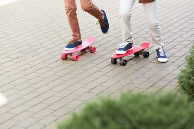 cropped view of two boys riding penny boards on pavement clipart