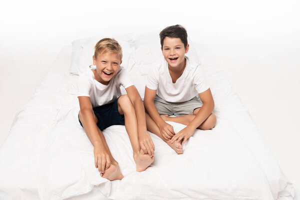 two happy brothers sitting on bed and smiling at camera on white background