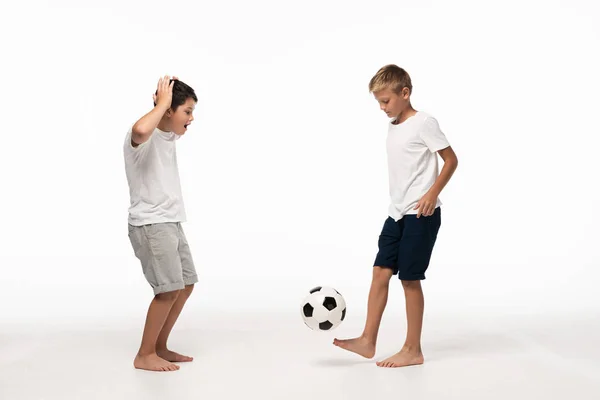 白い背景にサッカーボールで遊んでいる弟を見ながらすごいジェスチャーを示す興奮少年 — ストック写真