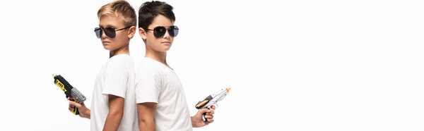panoramic shot of brothers in sunglasses standing back to back and holding toy guns while imitating gangsters isolated on white