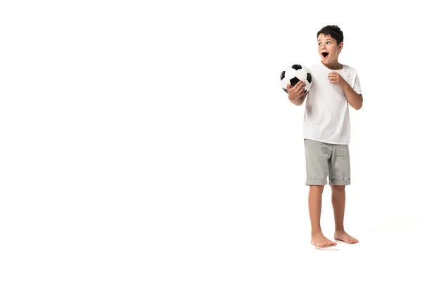 surprised boy holding soccer ball, looking away and pointing with finger on white background