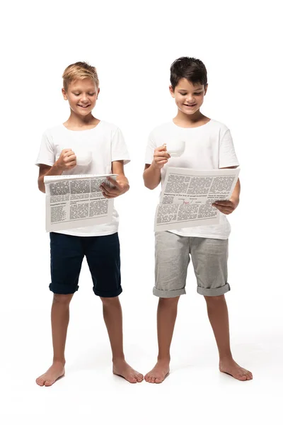 白い背景にコーヒーカップを持ちながら新聞を読む2人の笑顔の兄弟 — ストック写真