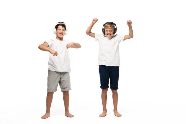 two cheerful brothers listening music in headphones and dancing on white background