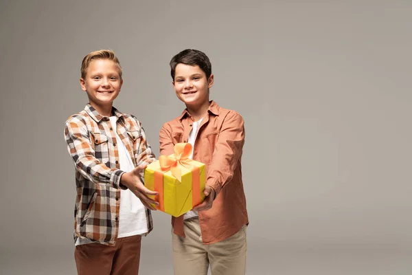 Δύο Ευτυχισμένα Αδέλφια Που Δείχνουν Κίτρινο Κουτί Δώρου Απομονωμένο Γκρι — Φωτογραφία Αρχείου
