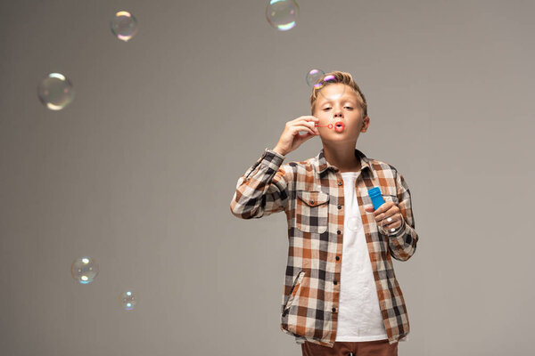 boy in checkered shirt blowing soap bubbles isolated on grey