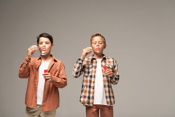 передний вид двух братьев, дующих мыльные пузыри, изолированные на сером
