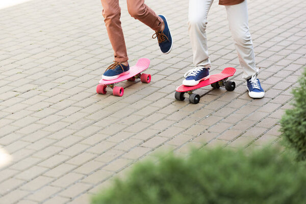 cropped view of two boys riding penny boards on pavement