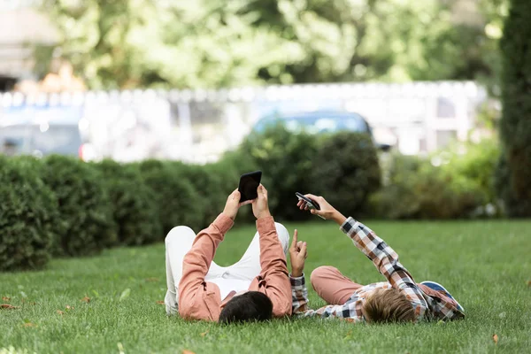 Kardeş Yeşil Çimlerde Uzanıyor Akıllı Telefonlar Kullanıyorlar — Stok fotoğraf