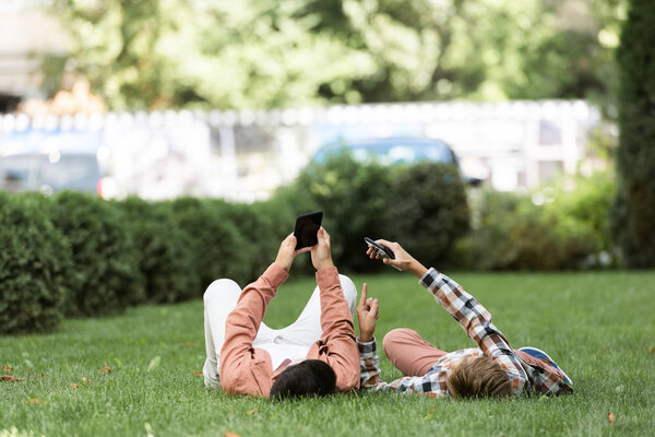 two brothers lying on green lawn on backs and using smartphones