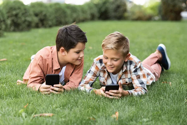 Dwóch Wesołych Braci Leżących Zielonym Trawniku Korzystających Smartfonów — Zdjęcie stockowe