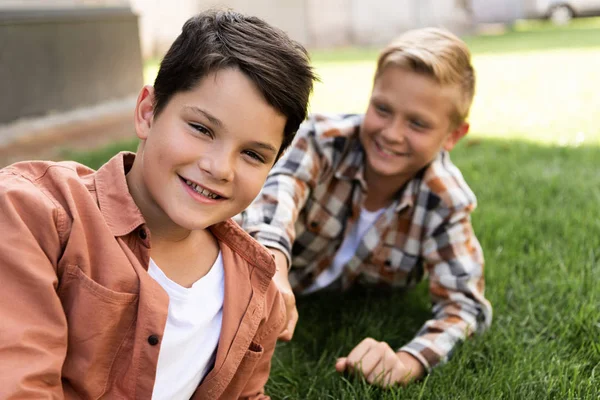 弟のそばの草の上に横になってカメラを見ている陽気な少年の選択的な焦点 — ストック写真