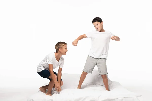 Sonriente Chico Sentándose Cama Cerca Hermano Imitando Boxeo Aislado Blanco — Foto de Stock