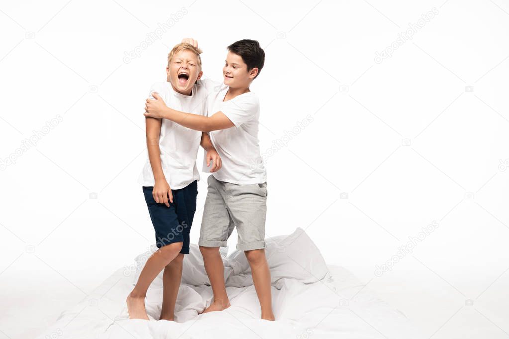 cheerful boy jokingly pulling hair of screaming brother isolated on white