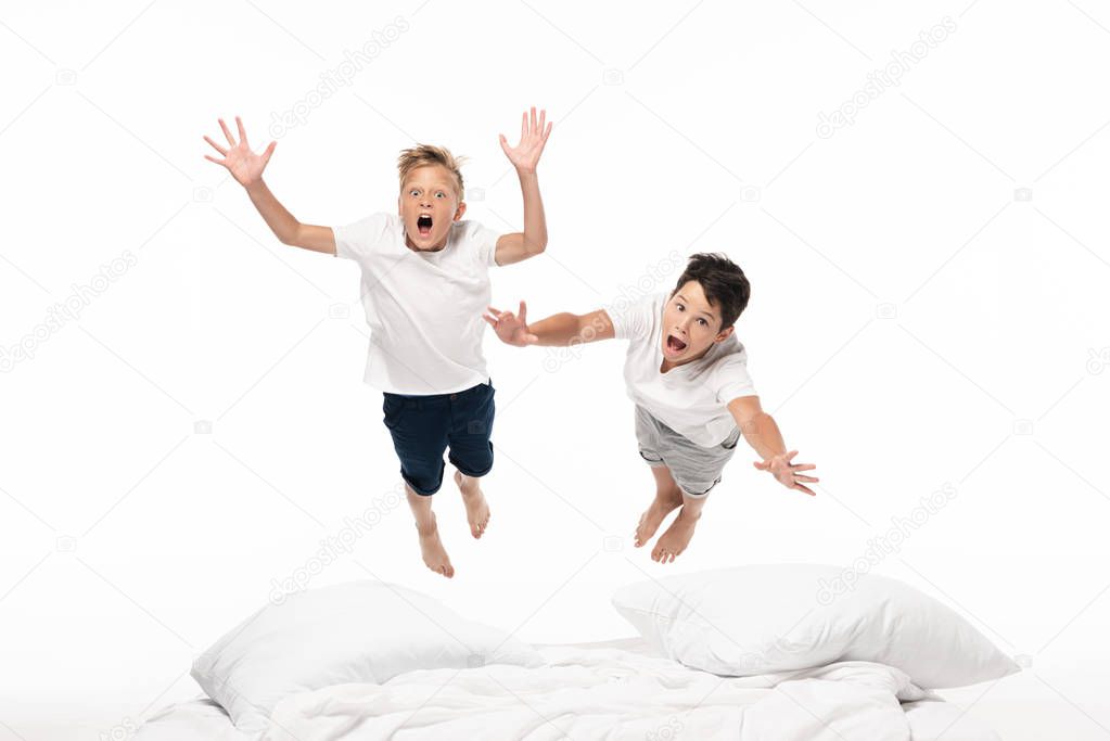 two excited brothers levitating over bed and looking at camera isolated on white