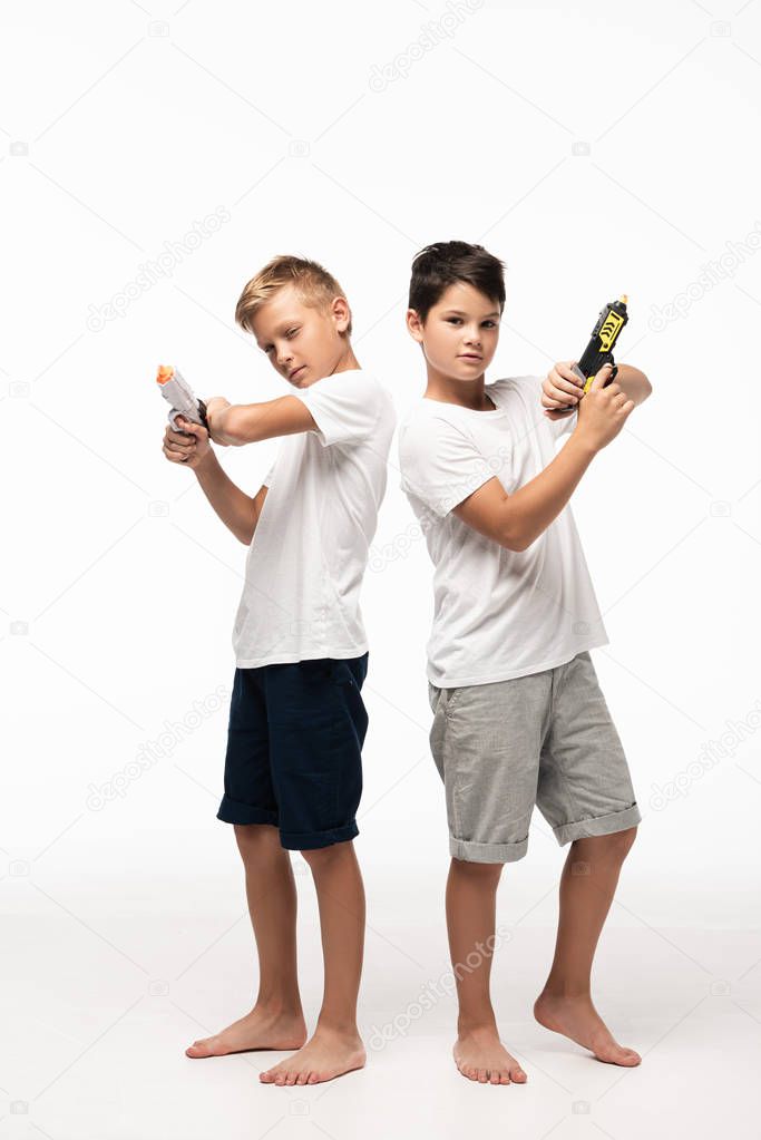 two brothers standing back to back, holding toy guns and looking at camera on white background