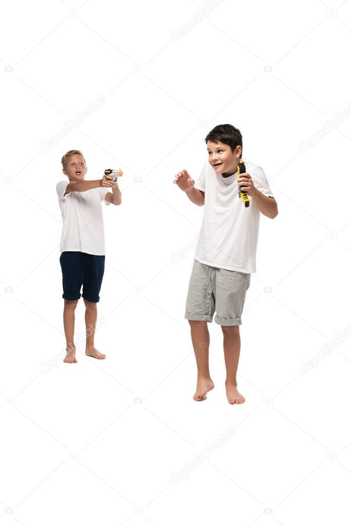 boy aiming with toy gun at scared brother on white background