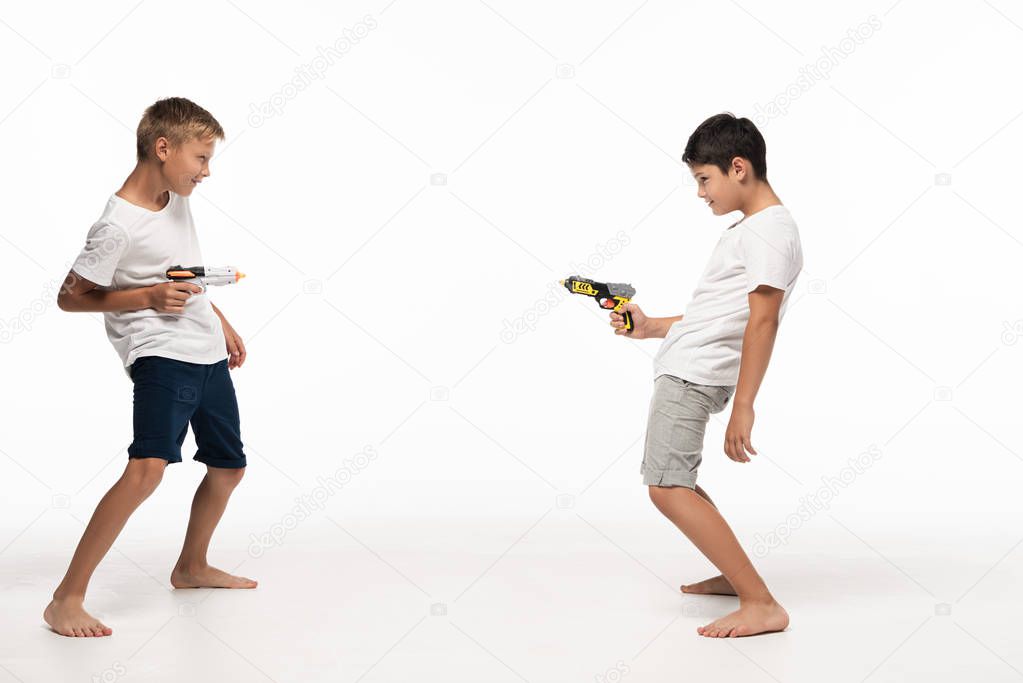 two brothers aiming at each other with toy guns on white background