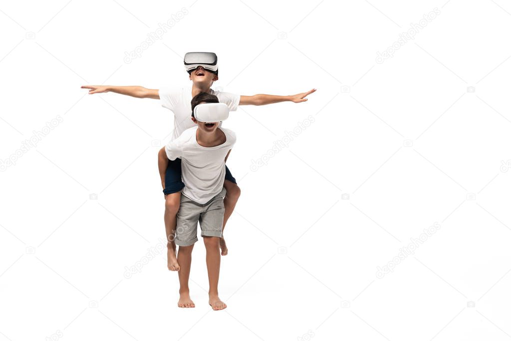 smiling boy using vr headset while piggybacking on brothers back and imitating flying on white background