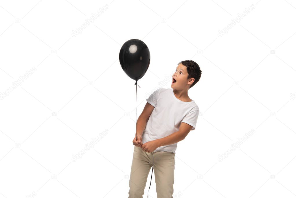 surprised boy looking at black balloon while standing isolated on white