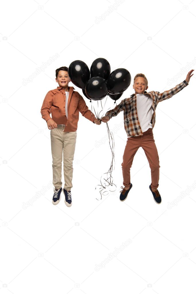 two excited boys flying with black festive balloons isolated on white